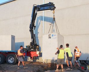 Four labourers crane lifting an SVC concrete pit into place.